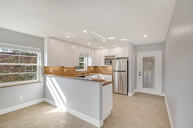 kitchen with white cabinets, kitchen peninsula, a textured ceiling, appliances with stainless steel finishes, and dark stone countertops