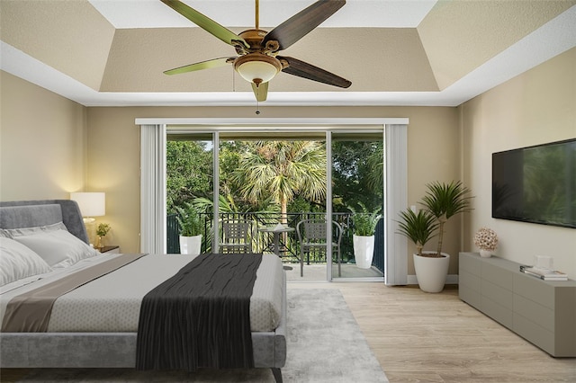 bedroom with access to exterior, ceiling fan, light hardwood / wood-style floors, and a raised ceiling