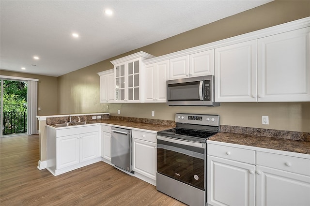 kitchen with white cabinetry, sink, stainless steel appliances, light hardwood / wood-style flooring, and kitchen peninsula