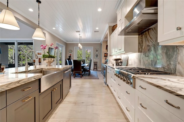 kitchen featuring pendant lighting, appliances with stainless steel finishes, light stone counters, white cabinets, and wall chimney exhaust hood