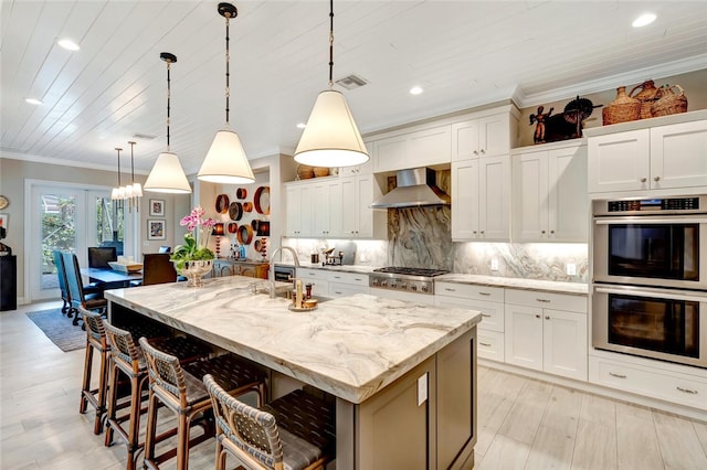 kitchen featuring stainless steel appliances, a kitchen island with sink, pendant lighting, and wall chimney exhaust hood