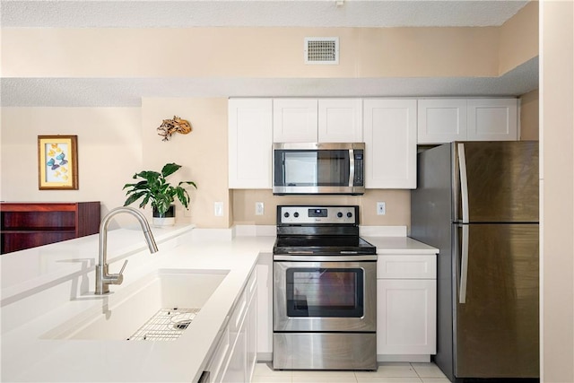 kitchen with sink, light tile patterned floors, a textured ceiling, white cabinets, and appliances with stainless steel finishes