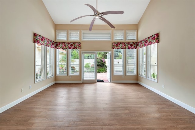 interior space with a towering ceiling, light wood-type flooring, a wealth of natural light, and ceiling fan