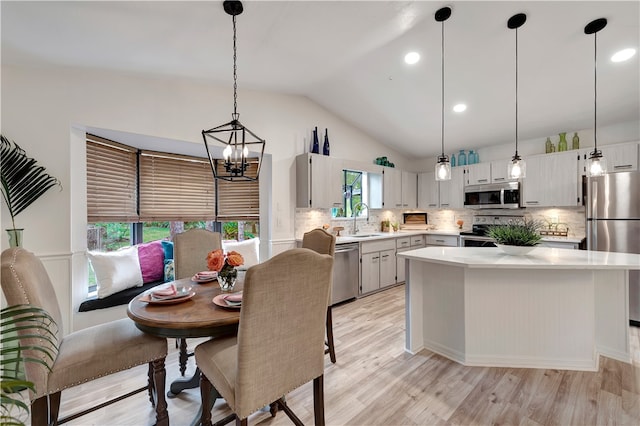 kitchen with vaulted ceiling, a kitchen island, sink, hanging light fixtures, and appliances with stainless steel finishes