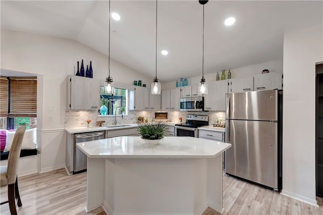 kitchen featuring lofted ceiling, a kitchen island, decorative light fixtures, stainless steel appliances, and sink