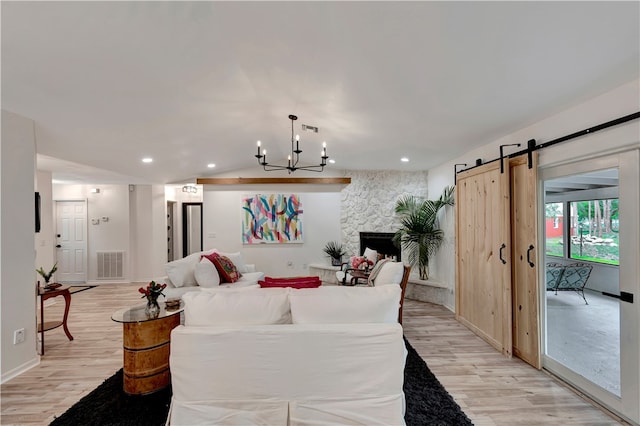 living room with a chandelier, lofted ceiling, a barn door, and light hardwood / wood-style flooring