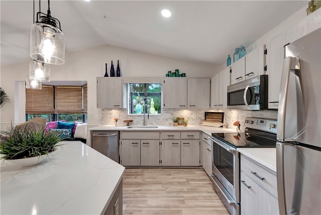 kitchen with decorative light fixtures, vaulted ceiling, backsplash, sink, and stainless steel appliances