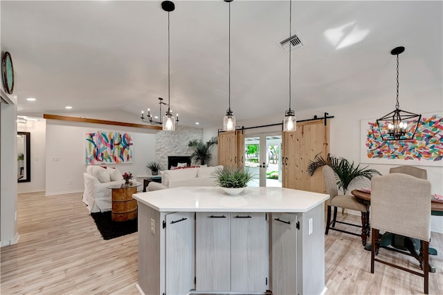 kitchen with a barn door, light wood-type flooring, lofted ceiling, a kitchen island, and pendant lighting