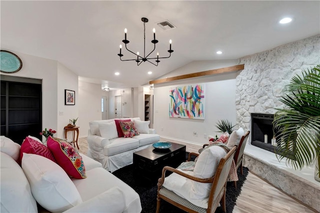 living room with vaulted ceiling, light hardwood / wood-style floors, a stone fireplace, and a notable chandelier