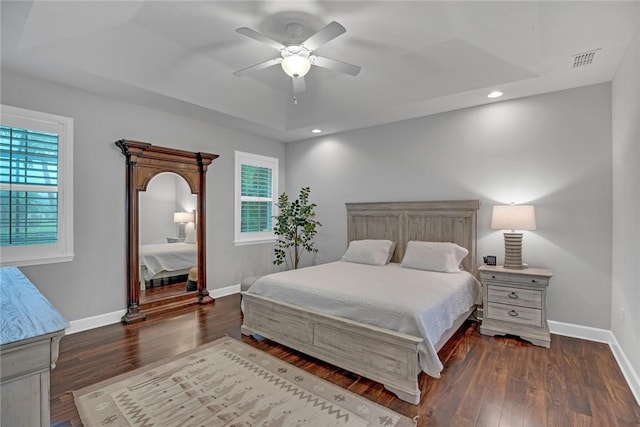 bedroom featuring ceiling fan, dark hardwood / wood-style floors, a raised ceiling, and multiple windows