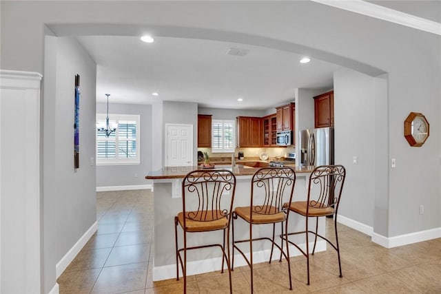 kitchen with hanging light fixtures, an inviting chandelier, a kitchen breakfast bar, light tile patterned flooring, and appliances with stainless steel finishes