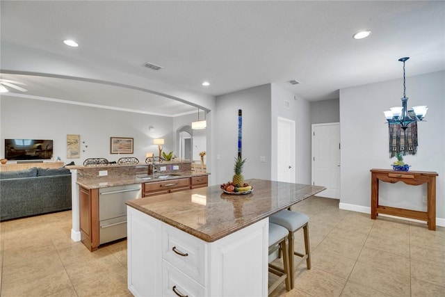 kitchen with white cabinets, pendant lighting, light stone countertops, and a spacious island