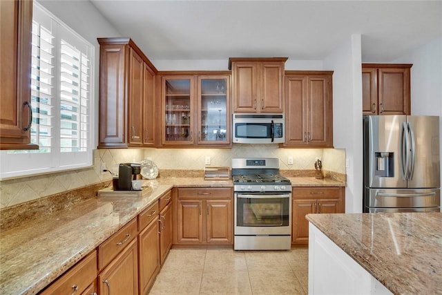 kitchen featuring backsplash, light stone counters, light tile patterned floors, and stainless steel appliances