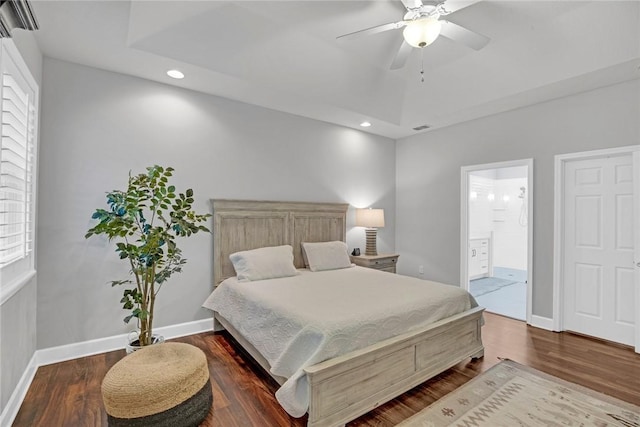 bedroom with ceiling fan, dark hardwood / wood-style floors, connected bathroom, and a tray ceiling