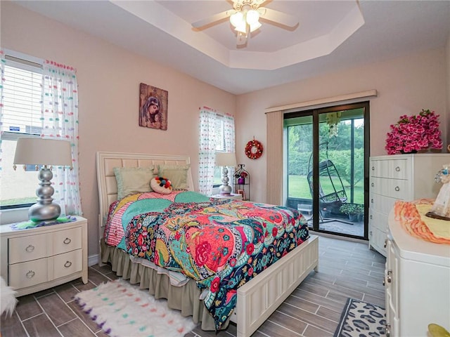 bedroom featuring access to exterior, multiple windows, a tray ceiling, and ceiling fan