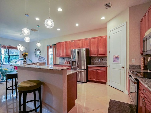 kitchen featuring tasteful backsplash, stainless steel appliances, hanging light fixtures, and an island with sink