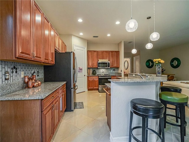 kitchen featuring a kitchen breakfast bar, decorative backsplash, light stone countertops, appliances with stainless steel finishes, and decorative light fixtures