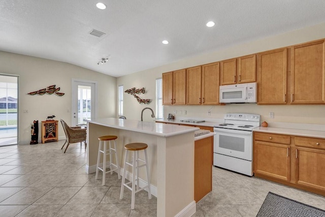 kitchen with lofted ceiling, white appliances, a breakfast bar area, a kitchen island with sink, and light tile patterned floors