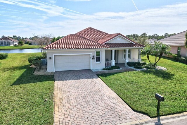 mediterranean / spanish home with a garage, covered porch, a water view, and a front lawn