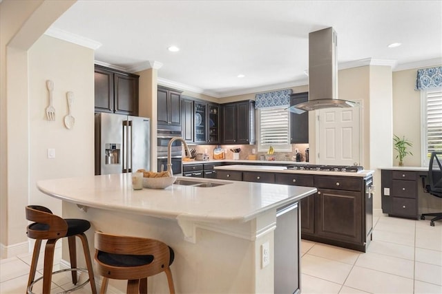 kitchen featuring dark brown cabinetry, a kitchen island with sink, stainless steel appliances, and island range hood