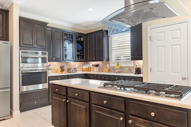 kitchen featuring dark brown cabinetry, stainless steel appliances, tasteful backsplash, island range hood, and light tile patterned floors