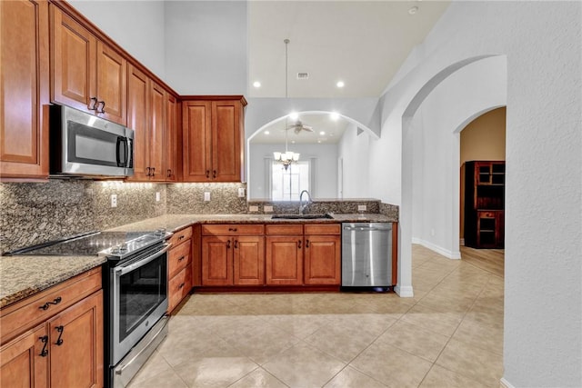 kitchen featuring brown cabinetry, tasteful backsplash, light stone counters, a sink, and stainless steel appliances