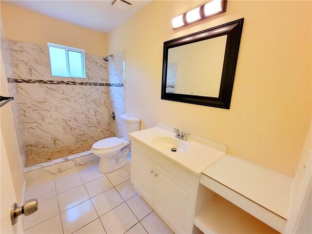 bathroom featuring vanity, toilet, a tile shower, and tile patterned flooring