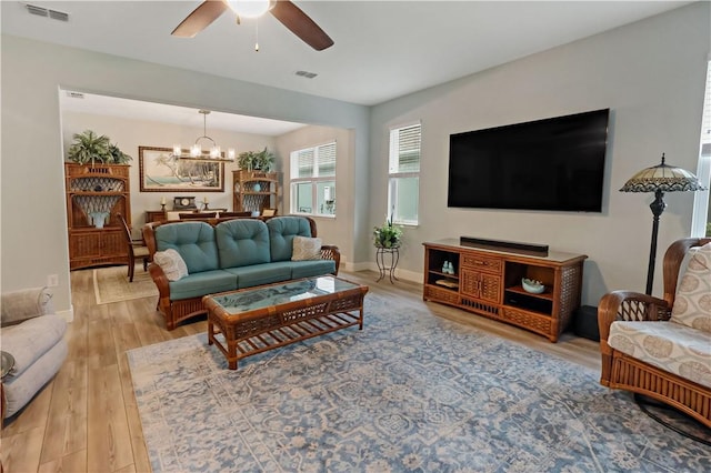 living room with ceiling fan with notable chandelier and light hardwood / wood-style floors