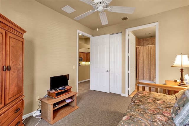 carpeted bedroom featuring a closet, ensuite bath, and ceiling fan