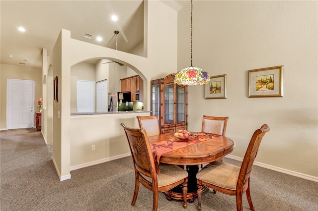 dining space featuring a towering ceiling and dark colored carpet