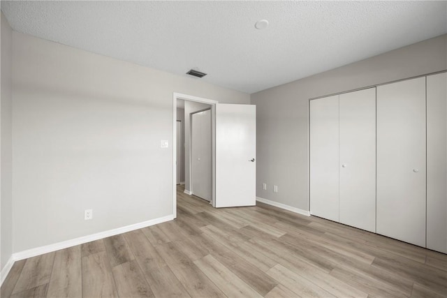 unfurnished bedroom featuring light wood-type flooring, a closet, and a textured ceiling