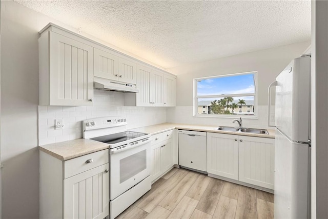 kitchen featuring sink, white cabinets, white appliances, light hardwood / wood-style floors, and a textured ceiling