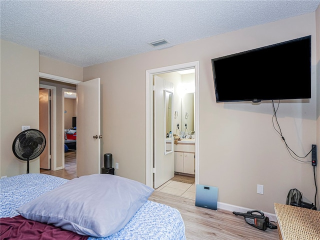 bedroom featuring connected bathroom, light hardwood / wood-style flooring, and a textured ceiling