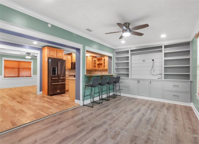 kitchen with a breakfast bar area, black fridge, crown molding, light wood-type flooring, and ceiling fan