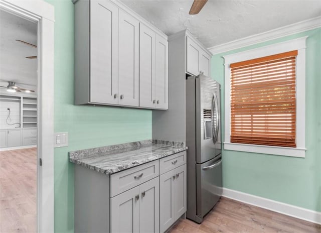 kitchen with light stone counters, light wood-type flooring, ornamental molding, stainless steel fridge, and ceiling fan