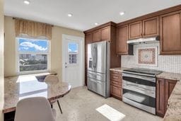 kitchen featuring stainless steel appliances, plenty of natural light, light stone counters, and decorative backsplash