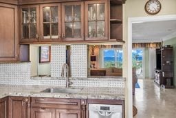 interior space with white dishwasher, light stone countertops, sink, and backsplash