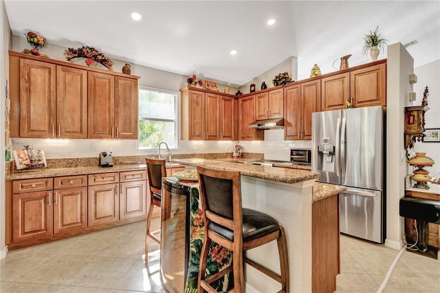 kitchen with stainless steel refrigerator with ice dispenser, light stone counters, a breakfast bar area, a center island, and lofted ceiling