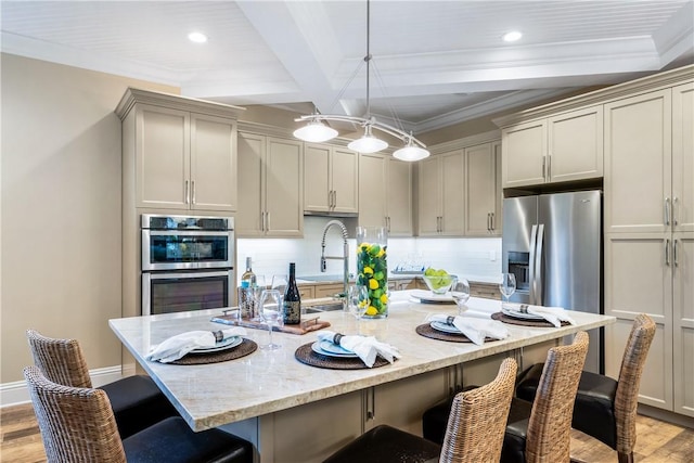 kitchen with appliances with stainless steel finishes, an island with sink, a kitchen bar, hanging light fixtures, and light stone countertops