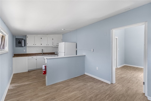 673 S Orlando Ave, Cocoa Beach, FL 32931 - kitchen featuring freestanding refrigerator, light wood-style floors, white cabinets, a peninsula, and a sink