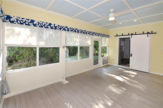 unfurnished sunroom with beam ceiling, a barn door, coffered ceiling, and ceiling fan