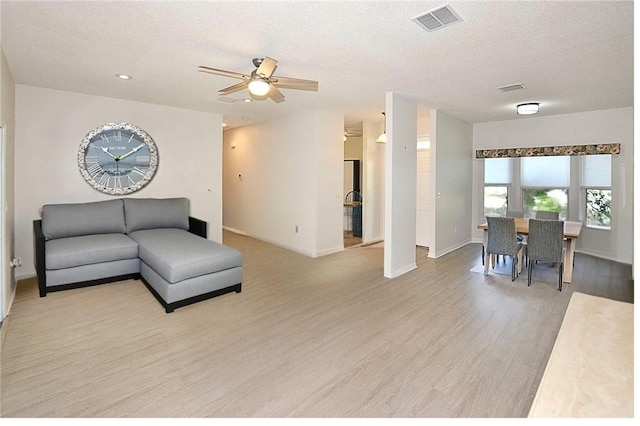 living room featuring ceiling fan, a textured ceiling, and light wood-type flooring