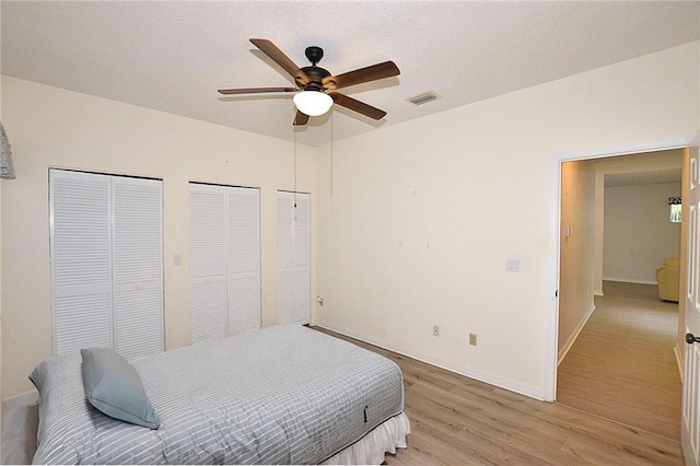 bedroom with multiple closets, ceiling fan, and light hardwood / wood-style flooring