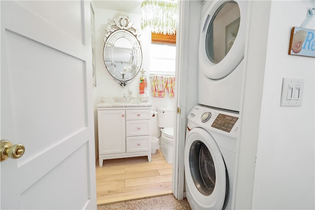 laundry room featuring stacked washer / drying machine, light wood-type flooring, and a healthy amount of sunlight