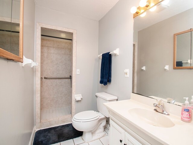 bathroom with toilet, vanity, tile patterned floors, and a tile shower