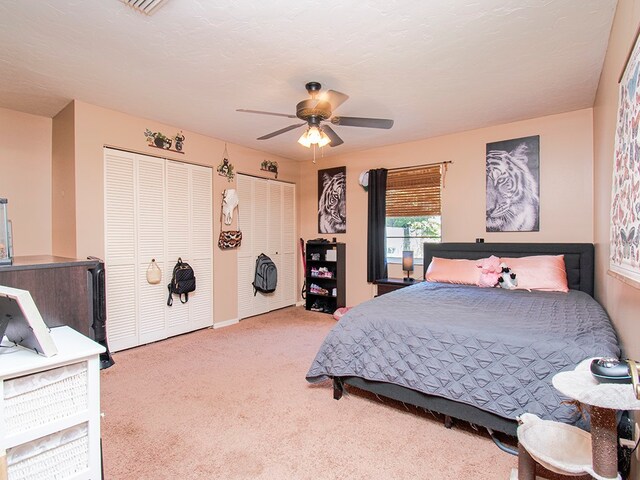 carpeted bedroom featuring multiple closets and ceiling fan