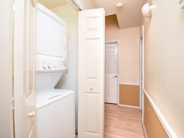 laundry area with light hardwood / wood-style floors and stacked washer / drying machine