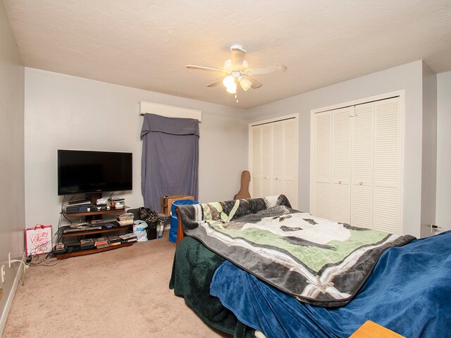 bedroom featuring a textured ceiling, carpet, ceiling fan, and two closets