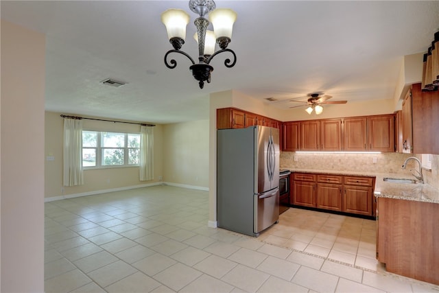 kitchen featuring stainless steel fridge, light stone countertops, decorative backsplash, sink, and ceiling fan with notable chandelier