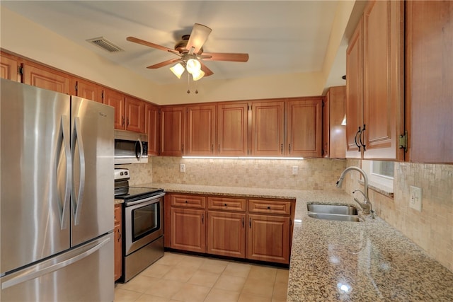 kitchen with appliances with stainless steel finishes, sink, backsplash, and light stone countertops